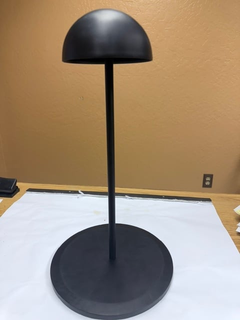 Black dome-shaped display stand with tall stem and round base on white surface against beige wall
