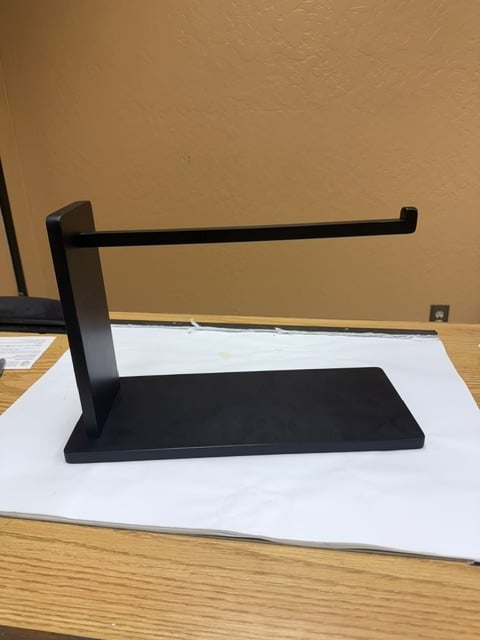 Black metal desk organizer with horizontal rod and base platform on white mat