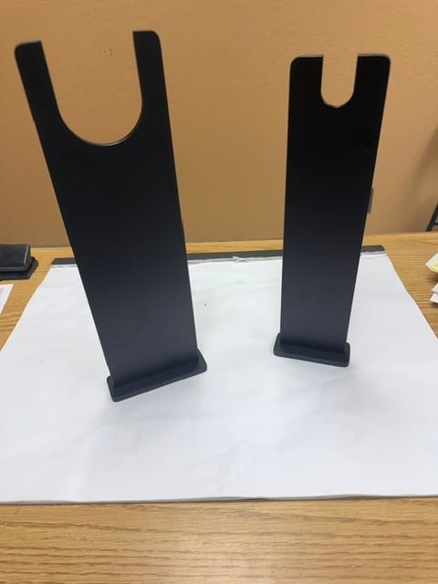 Two black metal display stands with U-shaped tops on a white surface against a tan wall
