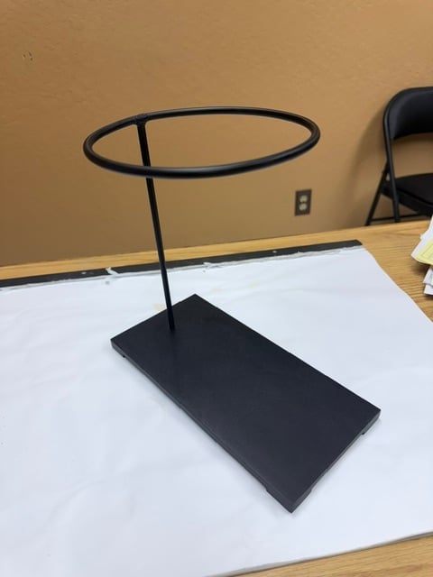Black metal jewelry display stand with oval ring holder on rectangular base, positioned on white surface