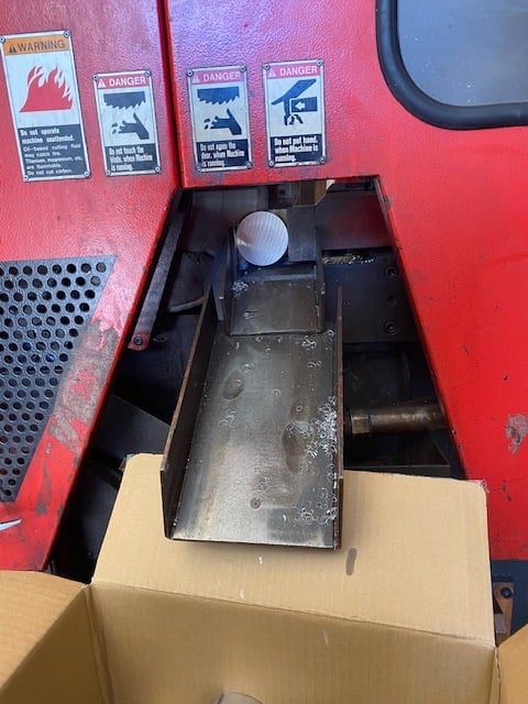 Open compartment in red machinery with black interior, cardboard box, and danger warning labels on metal surface above